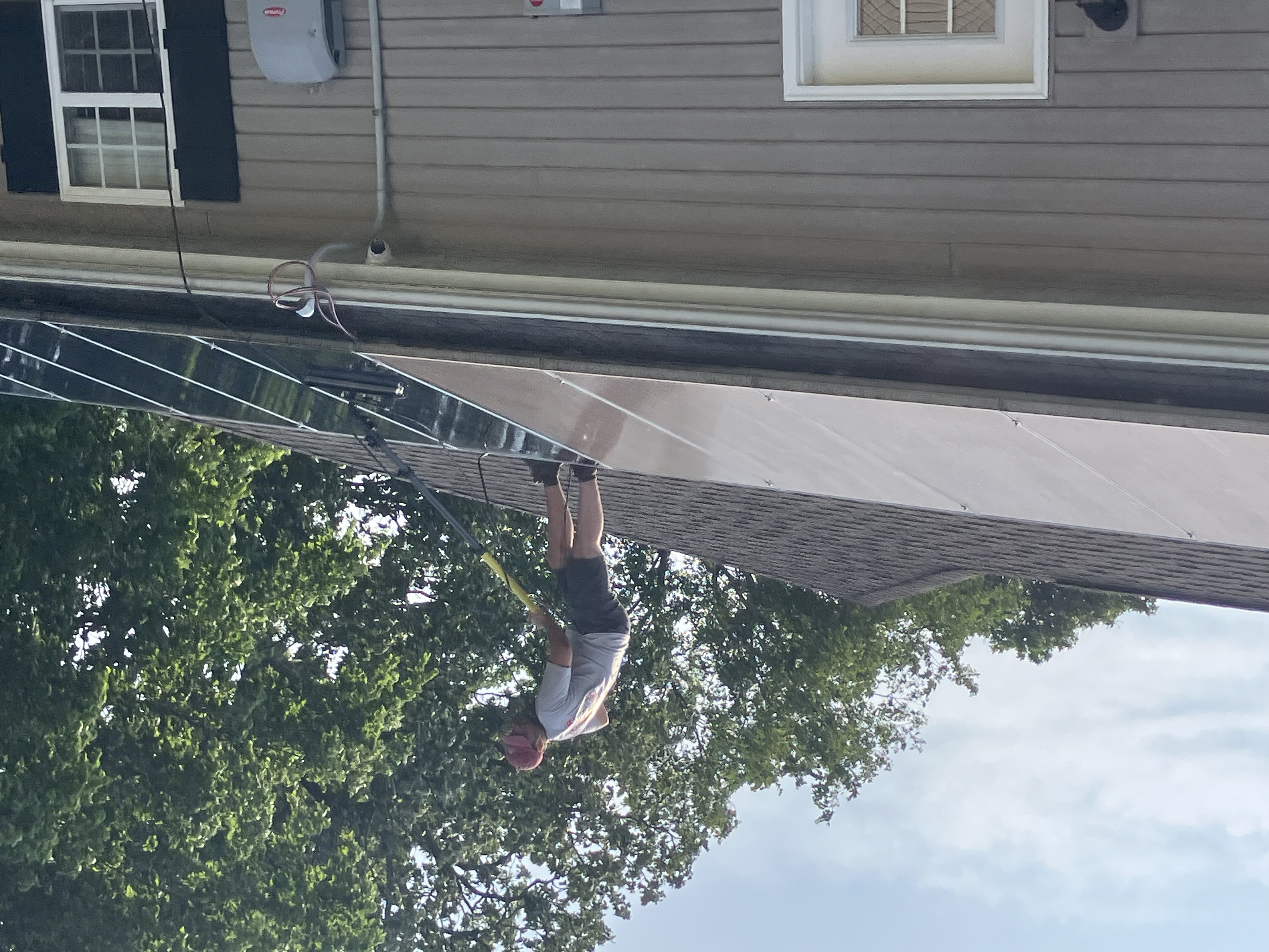 Technician on a roof using a soft-bristle pole brush on residential solar panels